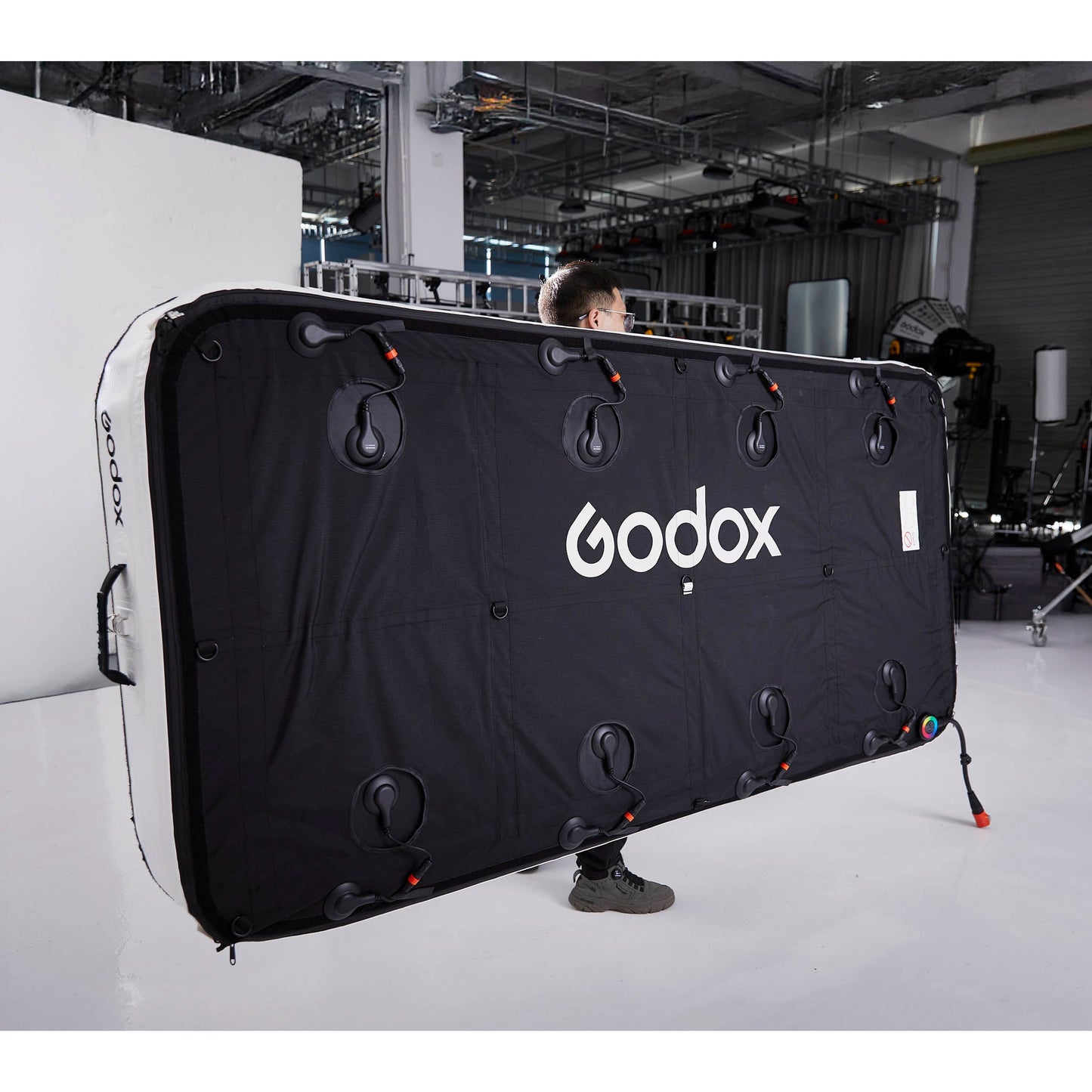 Gaffer carrying a Godox KNOWLED AM1600R-48K 4'x8' Inflatable RGB LED Light Mat showing the back of  the panel