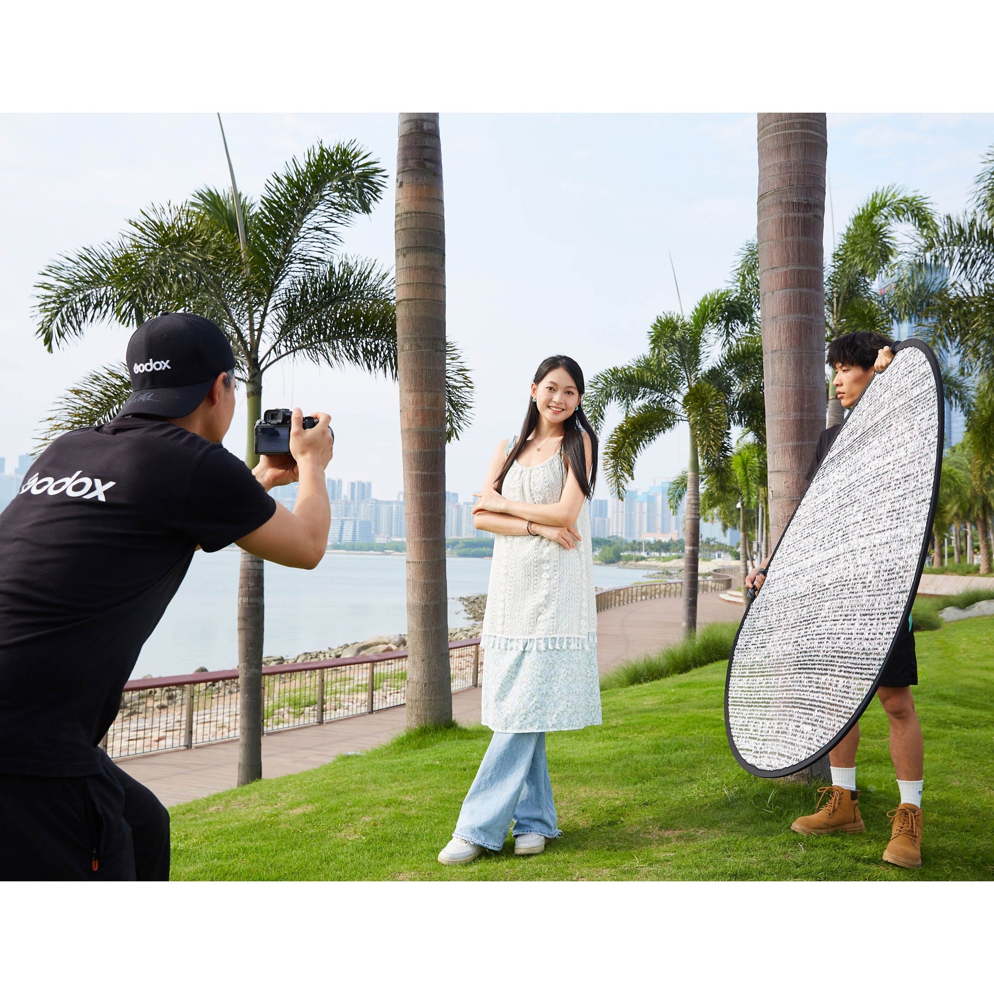 A Godox W-RFT130 130cm (52") Windproof Silver Collapsible Reflector being held by an assistant while a photographer takes photos of a model in a park
