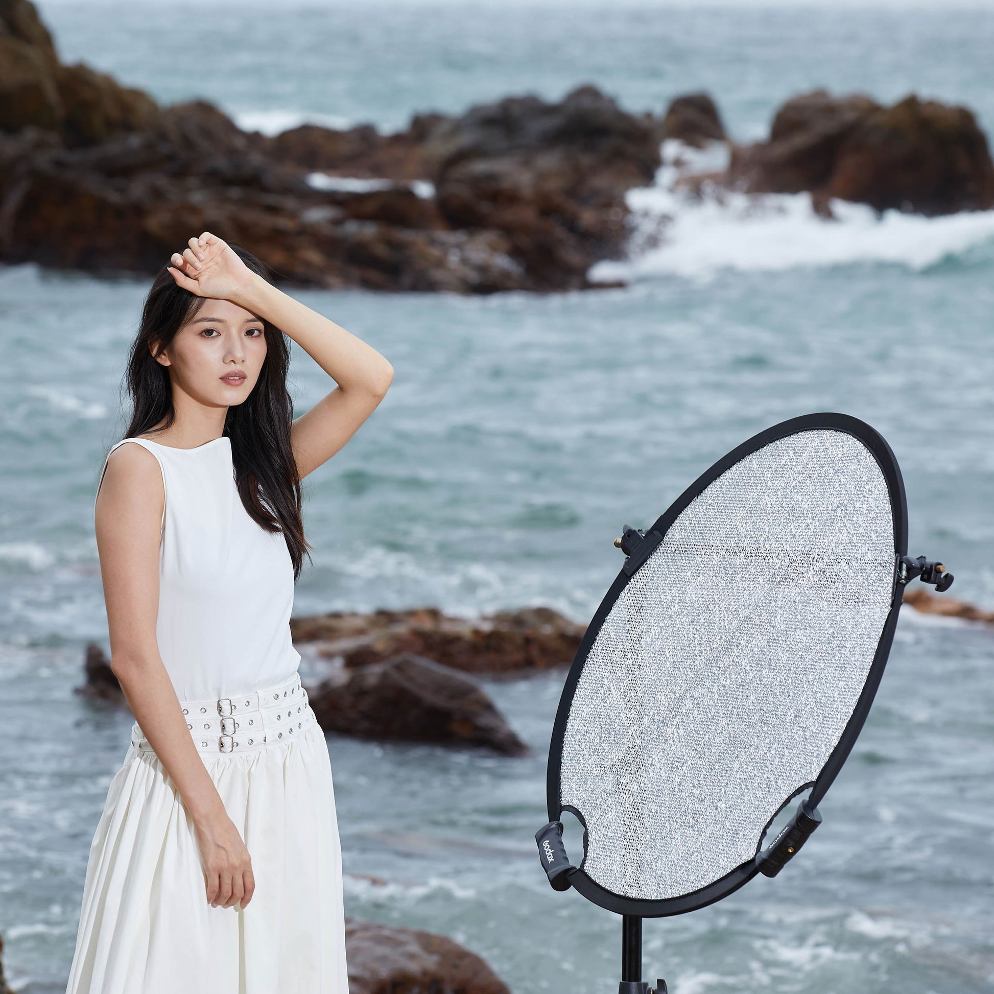 A Godox W-RFT80 80cm Collapsible Windproof Reflector mounted to a stand to bounce light onto a model by the sea