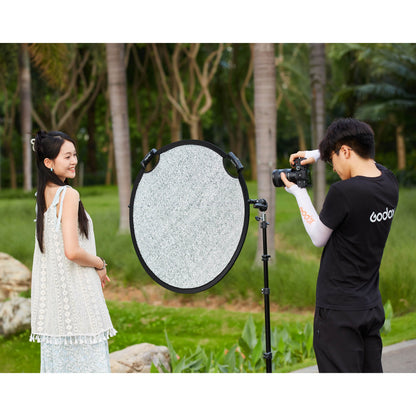A Photographer using a Godox W-RFT80 80cm Collapsible Windproof Reflector mounted to a stand to bounce light onto a model in a park