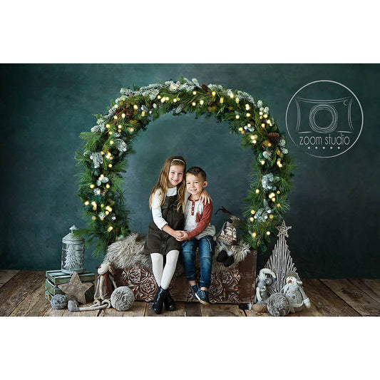 Two children sitting under a decorative arch with lights and greenery, surrounded by festive decorations.