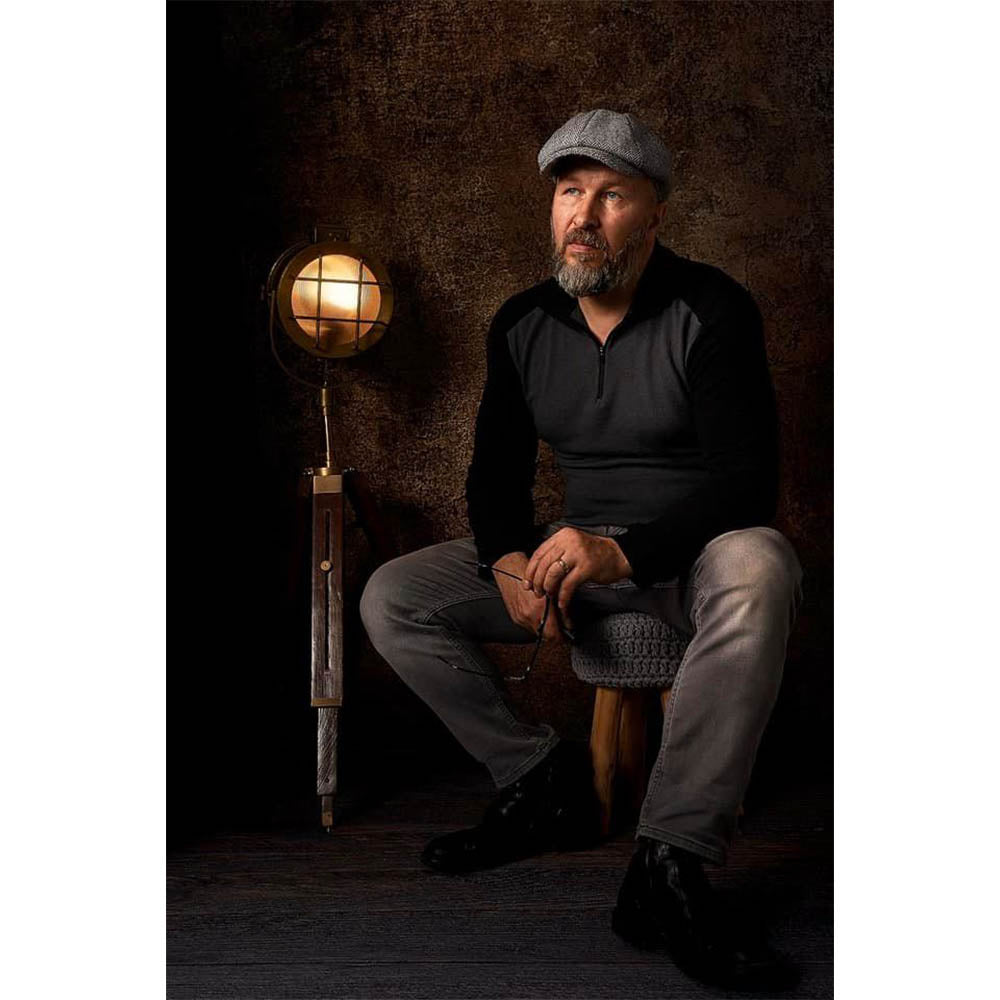 A man sitting on a stool with a lamp in front of a Kate Backdrops 2x3 Brown Concrete Textured Abstract Studio Photography Backdrop