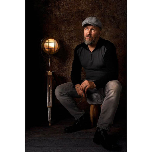 A man sitting on a stool with a lamp in front of a Kate Backdrops 2x3 Brown Concrete Textured Abstract Studio Photography Backdrop
