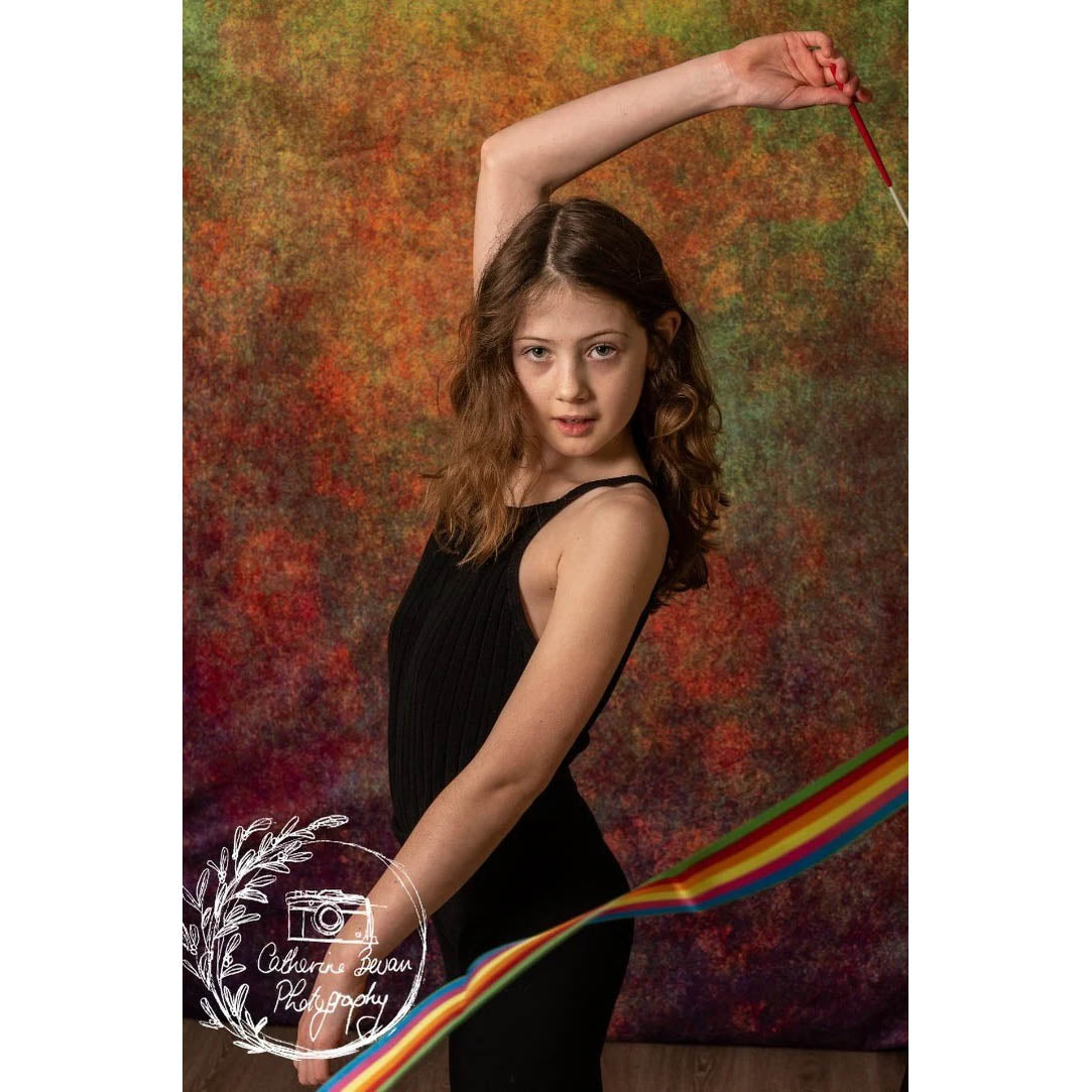 A photograph of a Rhythmic Gymnast in front of a Kate Backdrops 2x3 Abstract Rust Orange Green Textured Studio Backdrop