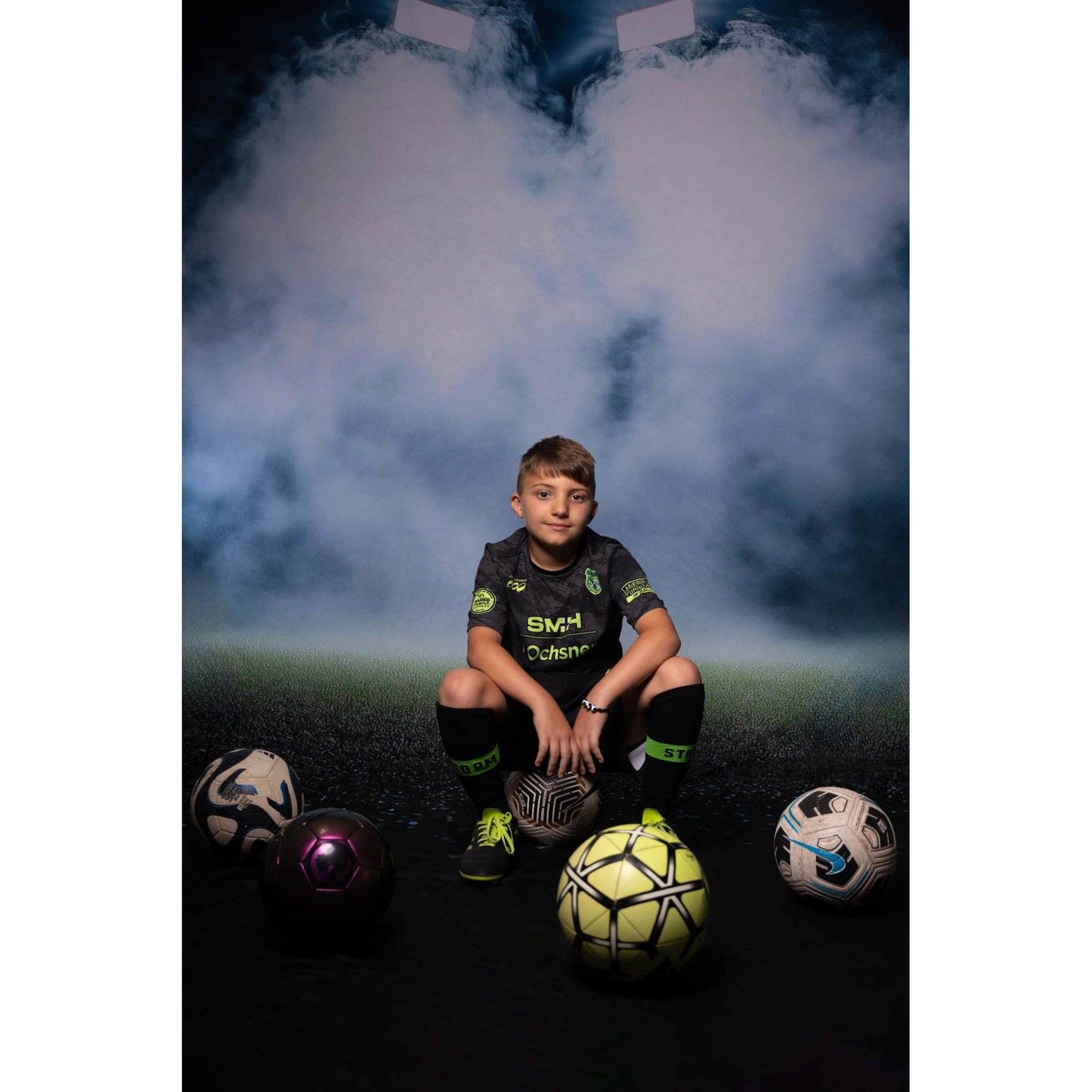 A you boy wearing football attire in front of a Sweep Sports Stadium Lighting Backdrop  sitting on a football