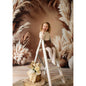 Young girl sitting on a ladder in front of pampas grass with a Sweep Boho Floral Arch Beige Backdrop in the background